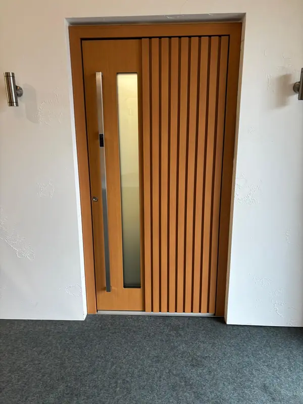 Haustür in Holzoptik mit vertikalen Stäben und Glaseinsatz in der Ausstellung